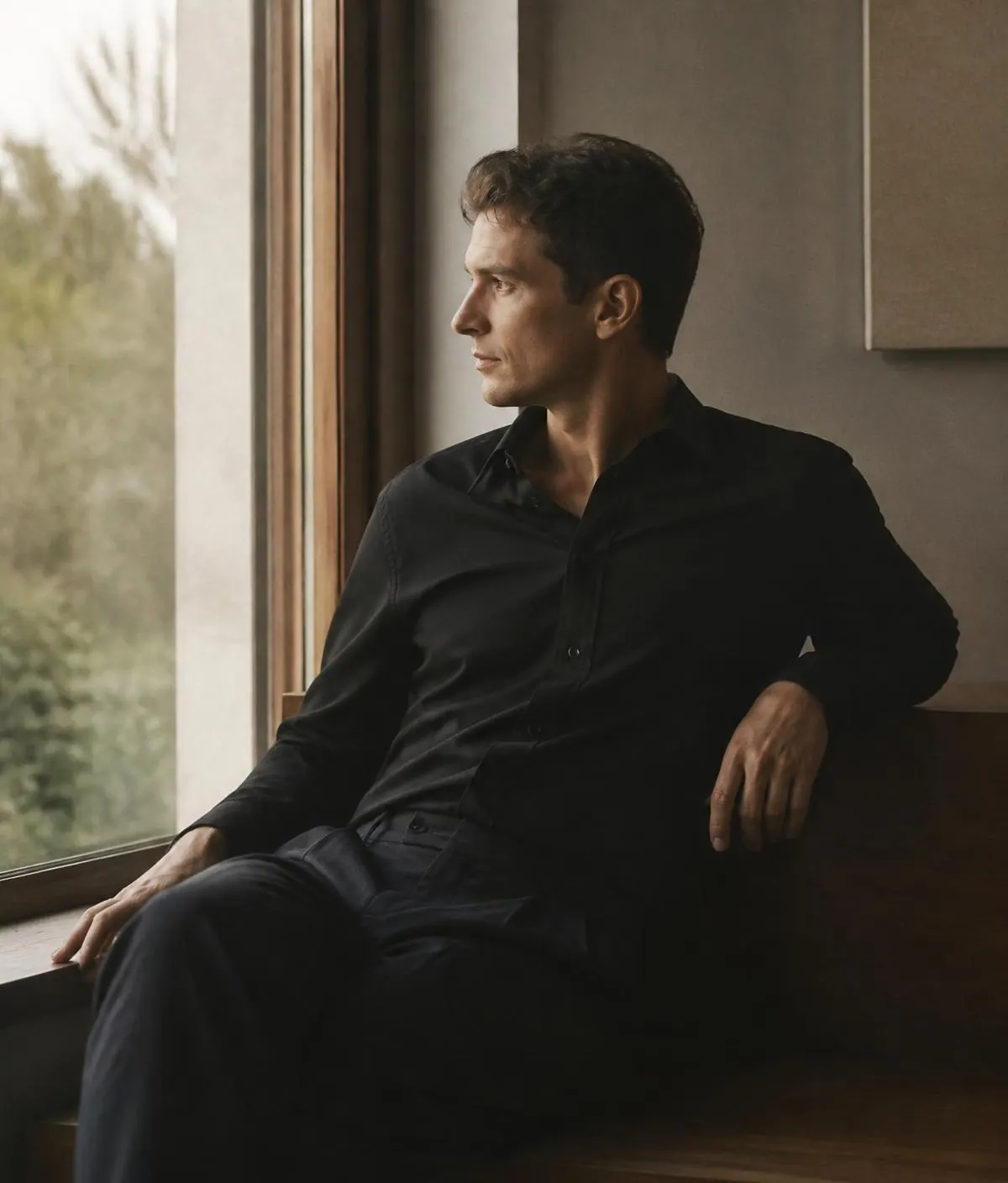 Man in a black shirt seated by a window